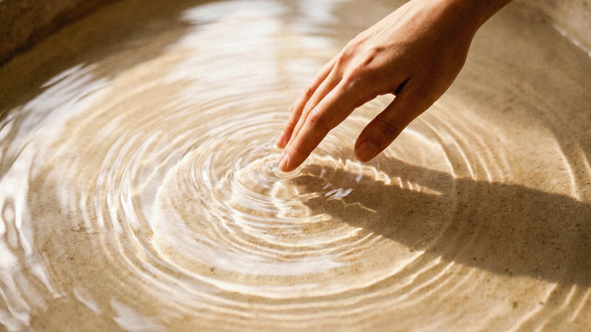 A hand gently touching sunlit water